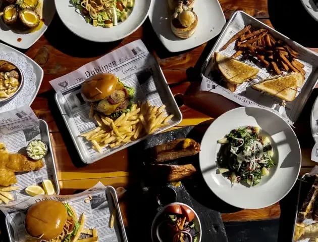 Flat-lay of a rustic table with burgers, fries, salads, and pub fare.