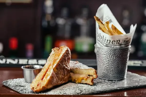 Powdered French toast, fries, and sauce on slate in a bar.