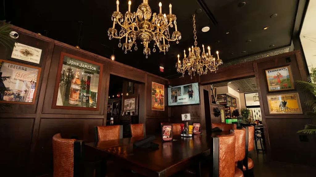 Dimly lit pub interior with dark wood, vintage posters, and gold chandeliers.