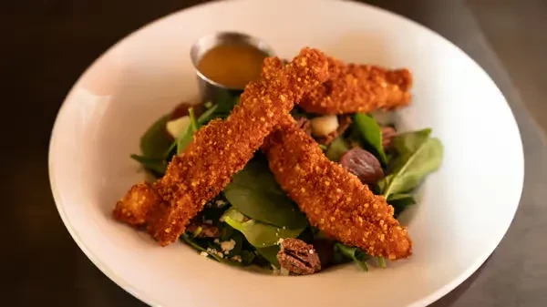 Crispy chicken strip salad with pecans and dressing in a white bowl.