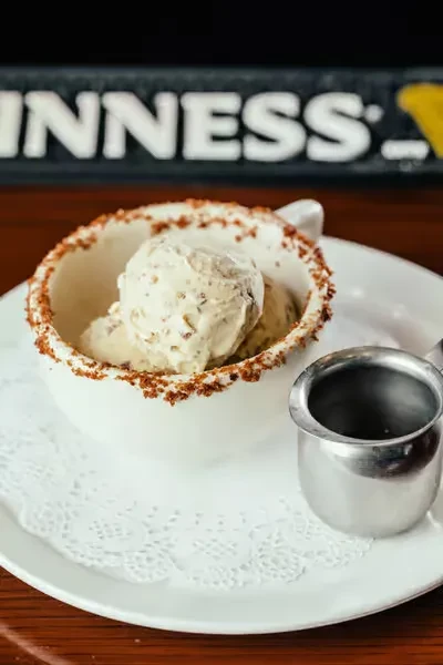 Ice cream with inclusions in white bowl, doily, blurred Guinness sign.