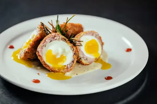 Halved Scotch eggs with runny yolks, sauces, and green herbs.