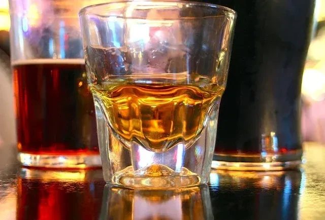A shot of whiskey, beer, and dark drink on a reflective bar.