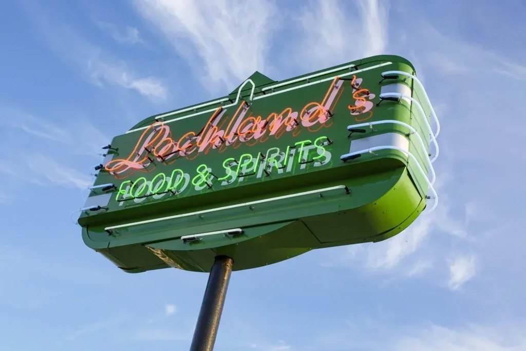 Retro green neon sign for "Rockland's Food & Spirits" against blue sky.