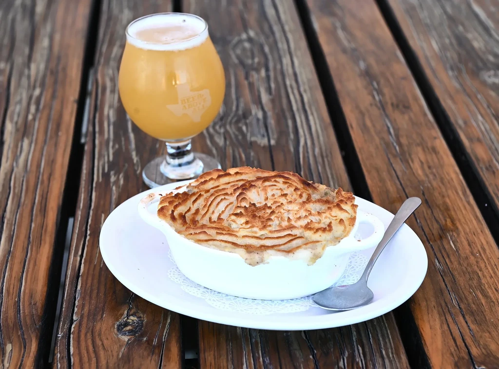 Baked golden-brown dish and Texas beer on a rustic wood table.