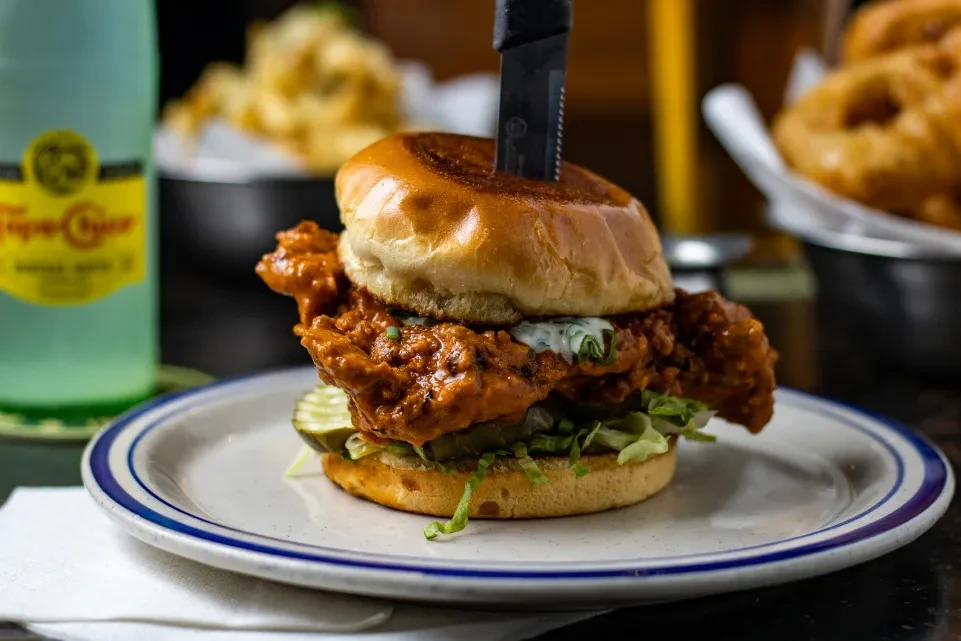 Crispy fried chicken sandwich with hot sauce, ranch, lettuce, pickles, knife.