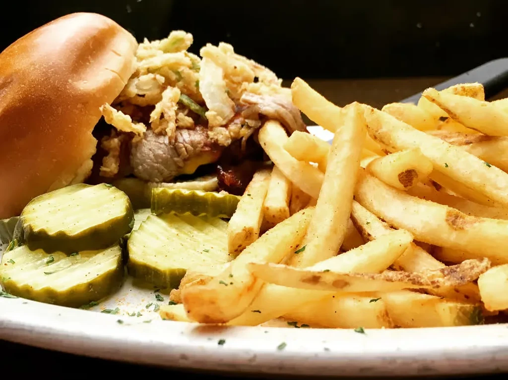 Burger topped with crispy onions, fries, and pickles on a white plate.