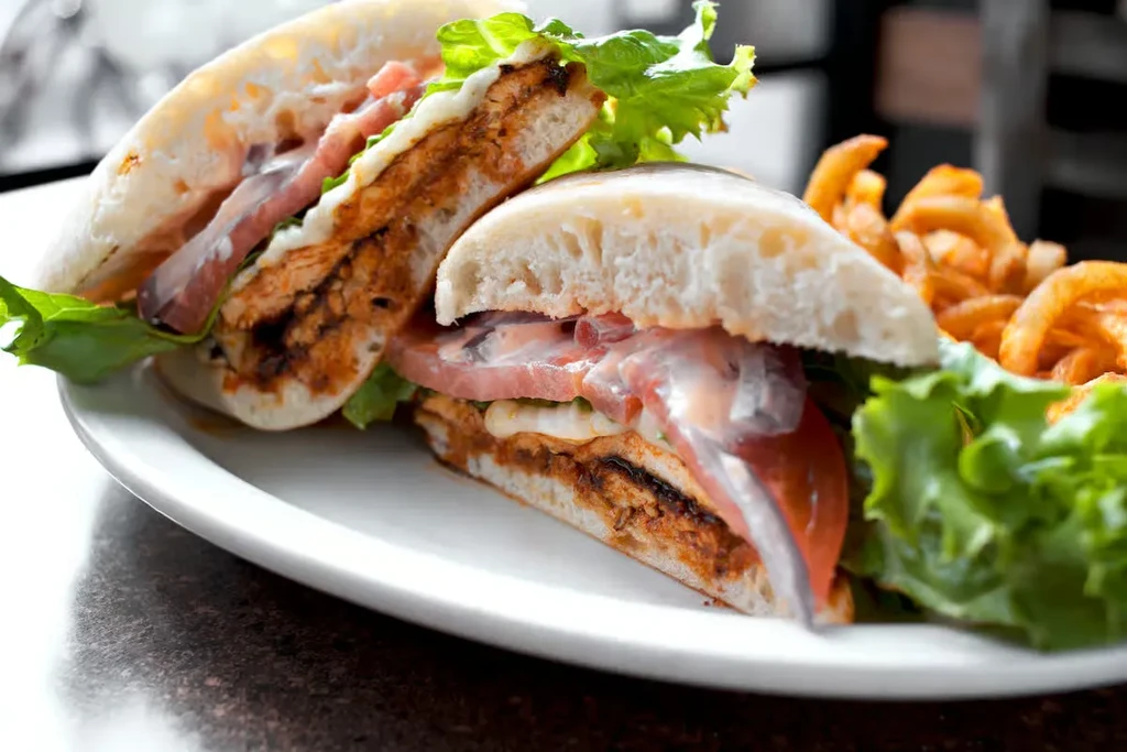 Grilled chicken sandwich cut in half, served with curly fries and lettuce.