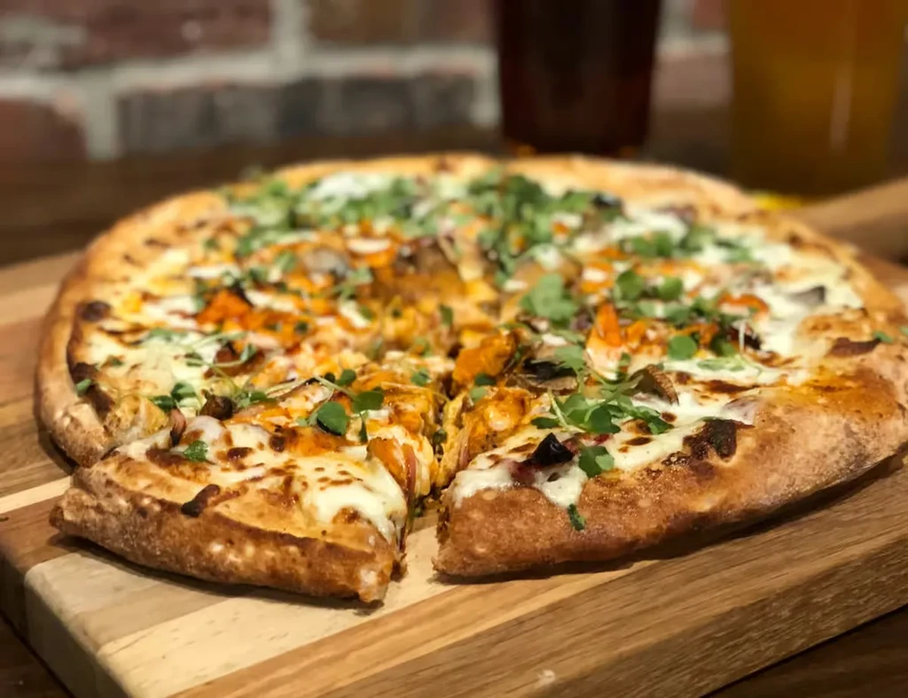 Freshly baked pizza with chicken, cheese, mushrooms, herbs on a wood board.