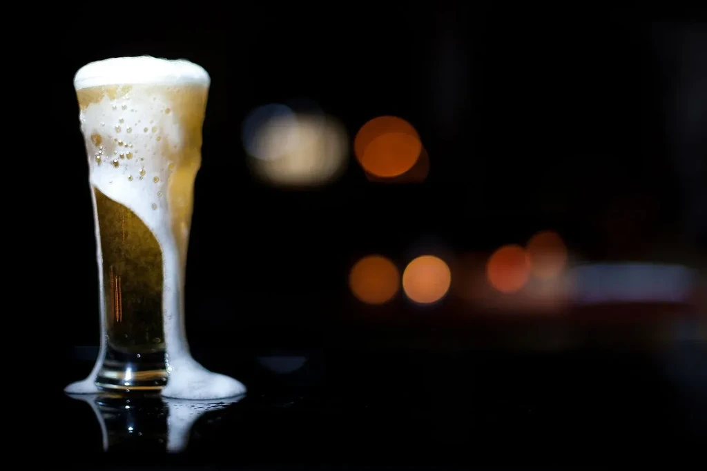 Glass of golden amber beer with overflowing frothy head.