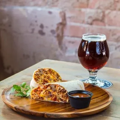Burrito halves, dipping sauce, and beer on a wooden table.