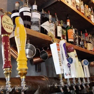 Close-up of bar beer taps and liquor bottles on wooden shelves.