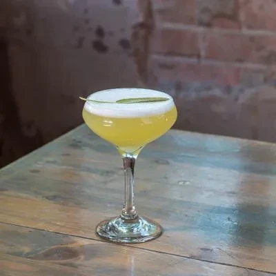 Yellow cocktail in a coupe glass with foam and green leaf.