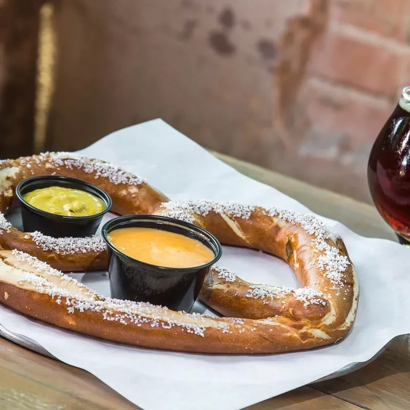 Golden-brown salted pretzel with mustard and cheese sauces.