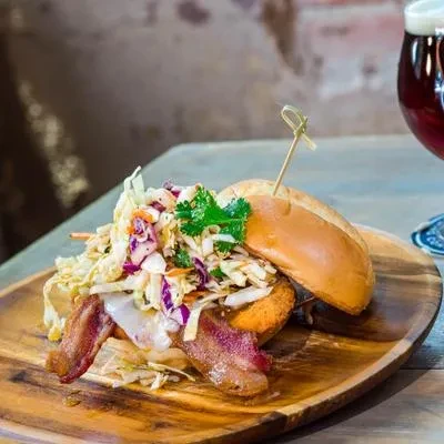 Close-up of a gourmet sandwich with coleslaw, bacon, and melted cheese.