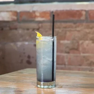 Iced light blue drink with lemon, straw, on table, brick background.