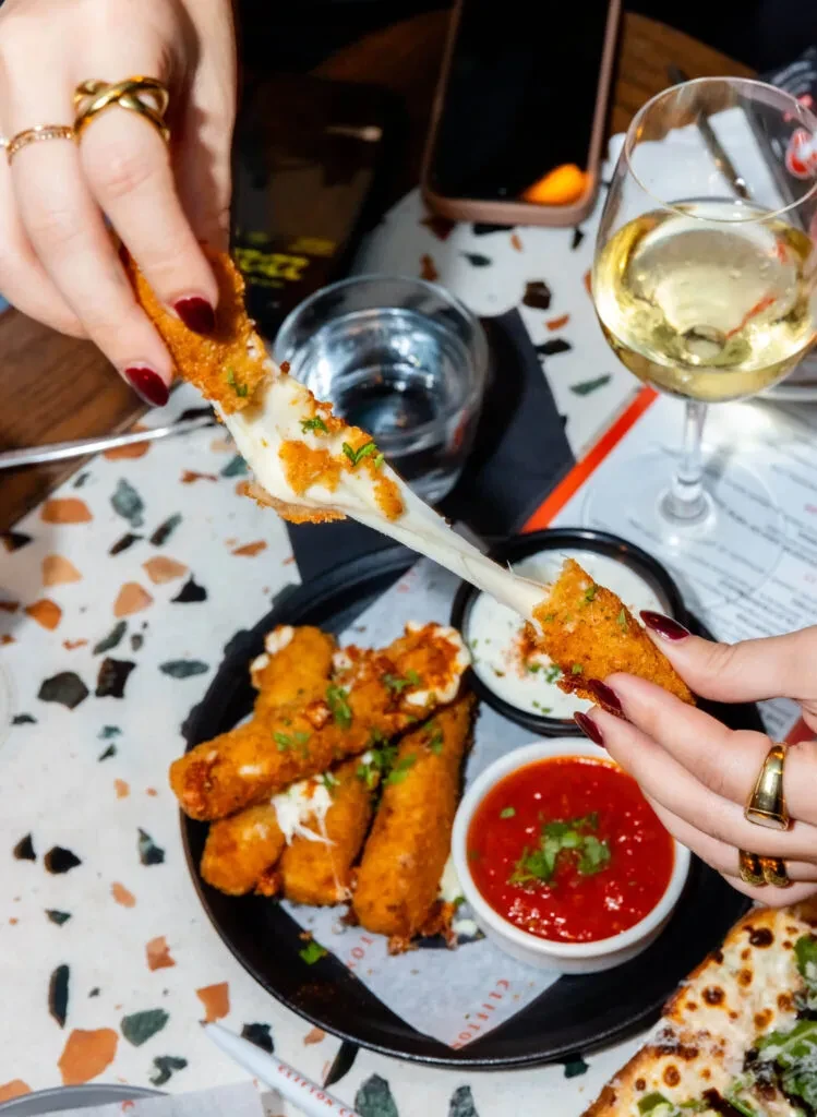 Hands pulling a mozzarella stick, showing stretchy cheese and sauces.