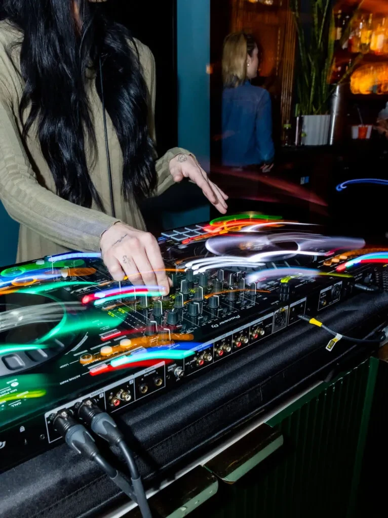 Close-up of hands operating a DJ mixer with colorful blurred lights.