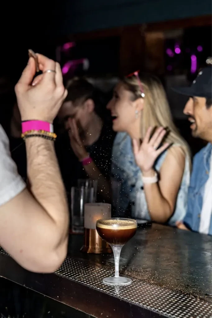 Dark cocktail with foam, blurred people in a lively, dim bar.