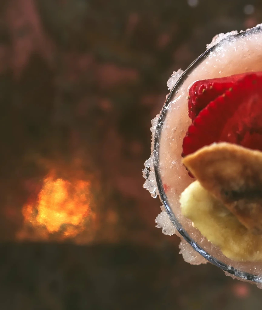 Pink cocktail with strawberries, sugared rim, and warm blurred background.