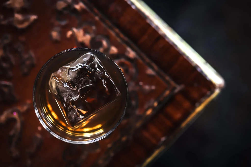 Top-down view of amber drink with large, cracked ice on wood.