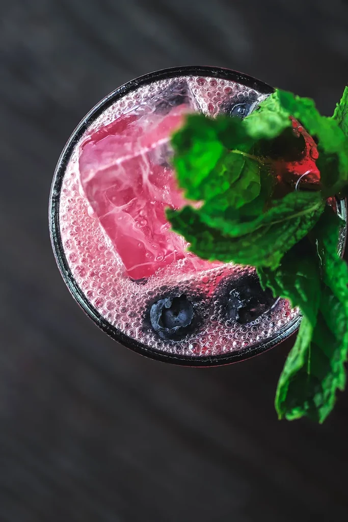 Frothy pink drink with reddish ice, blueberries, and fresh mint.