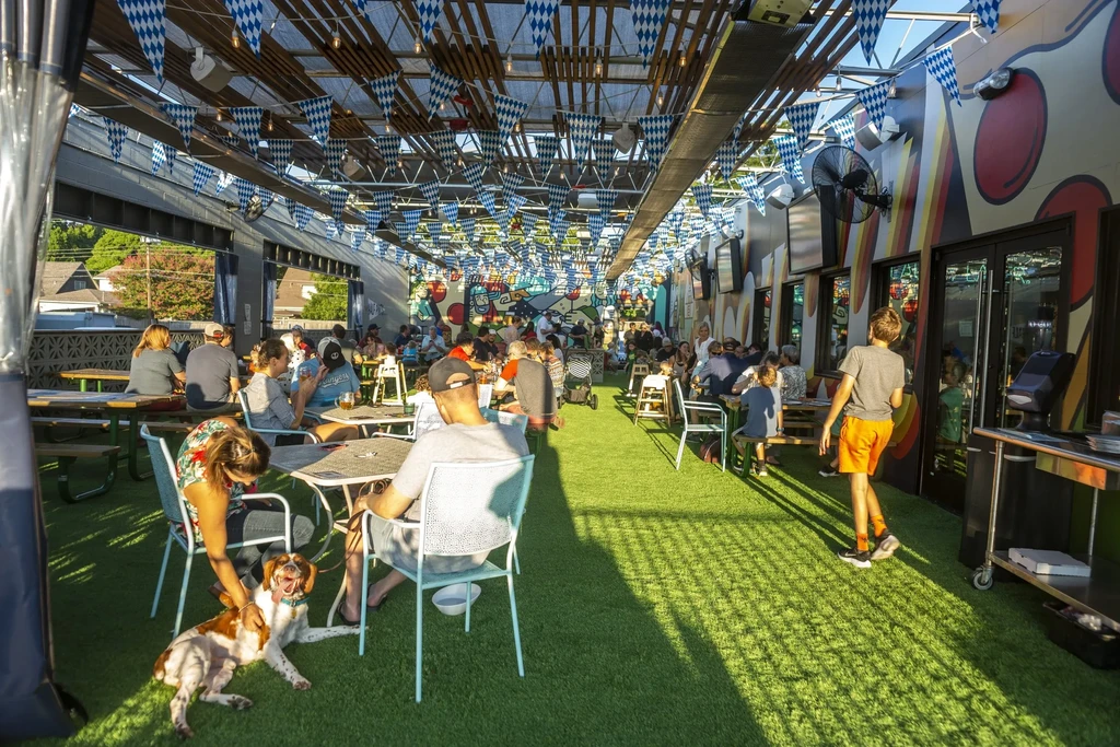 Bustling outdoor restaurant patio with diners, colorful banners, and a dog.