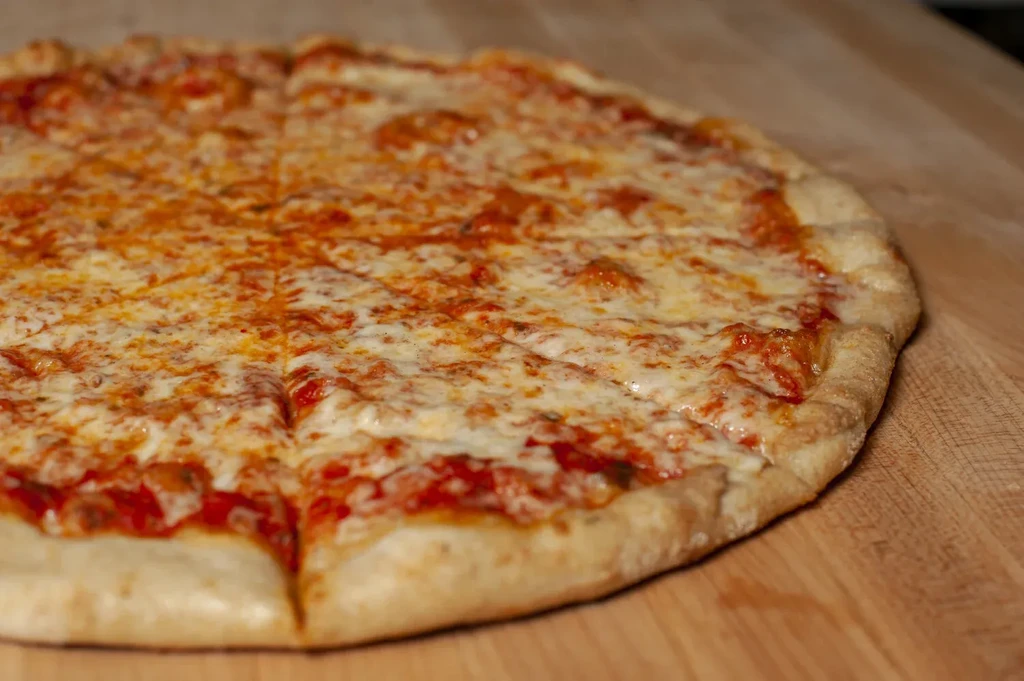 Sliced cheese pizza with melted white cheese and golden crust on wood.
