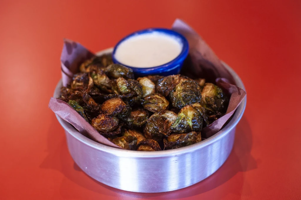 Roasted Brussels sprouts in a metal bowl with white dipping sauce.