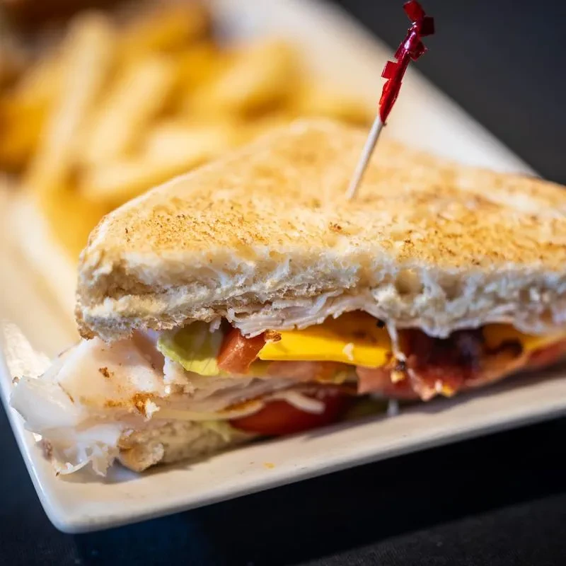 Toasted club sandwich halves with turkey, cheese, bacon, and fries.