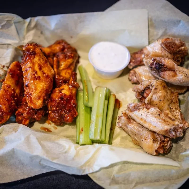 Basket of sauced and dry-rubbed chicken wings with celery and dip.