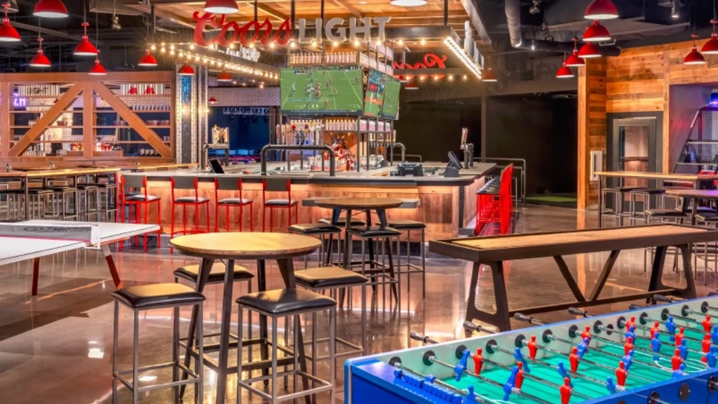 Vibrant, empty sports bar with large bar, TVs, and games.