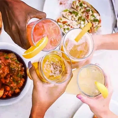 Diverse hands raise four distinct drinks in a toast.
