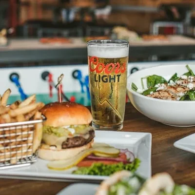 Close-up of gourmet burger, fries, Coors Light beer, chicken salad.