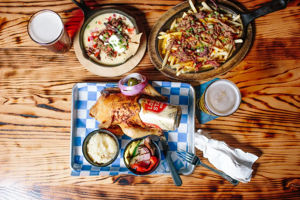 Overhead view of beer can chicken, loaded fries, queso, and beer.