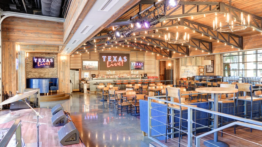 Empty modern rustic-industrial venue with stage, bar, and 'TEXAS Live!' screens.