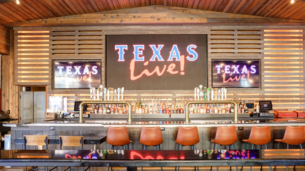 Dark bar interior with taps, stools, and "TEXAS Live!" screens.