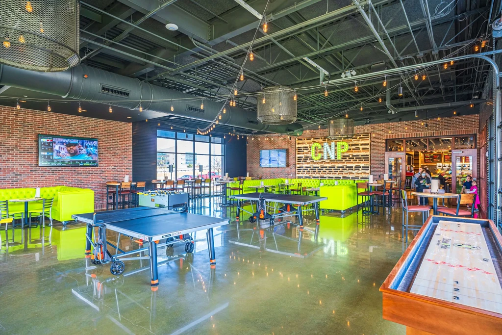 Spacious industrial-chic venue with neon-green booths, games, and TVs.