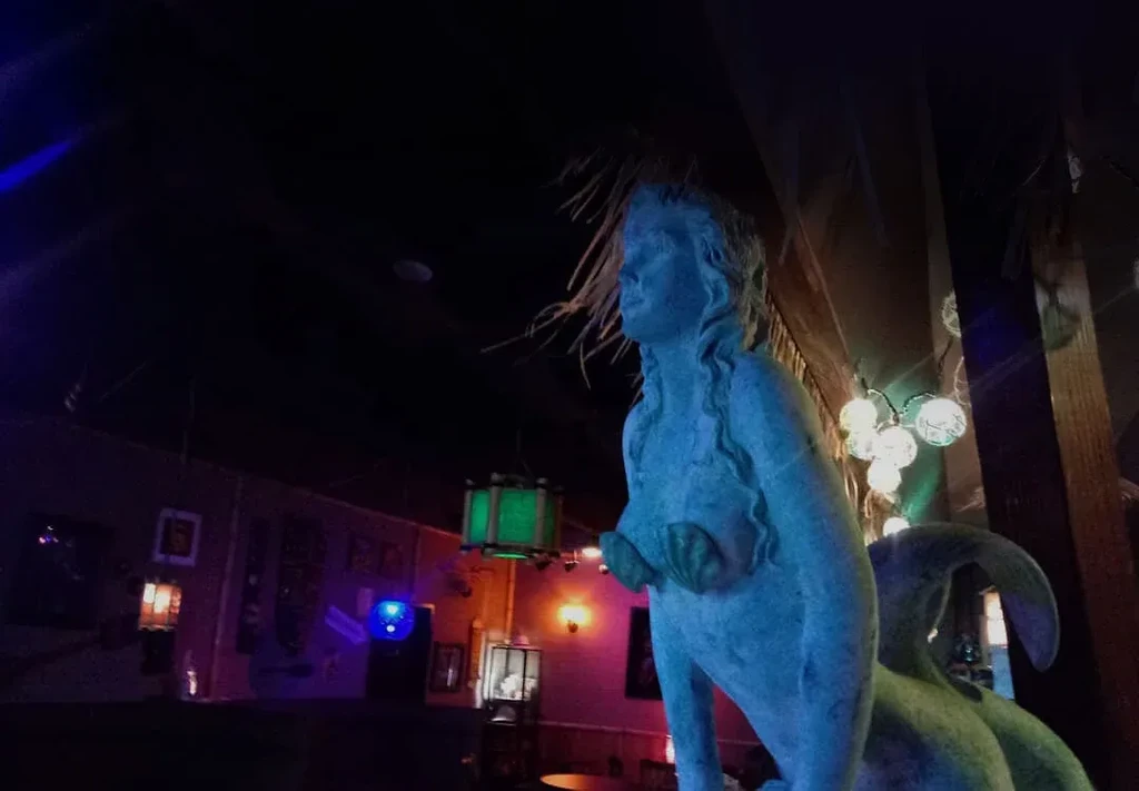 Mermaid statue glowing blue in a dimly lit, atmospheric bar.