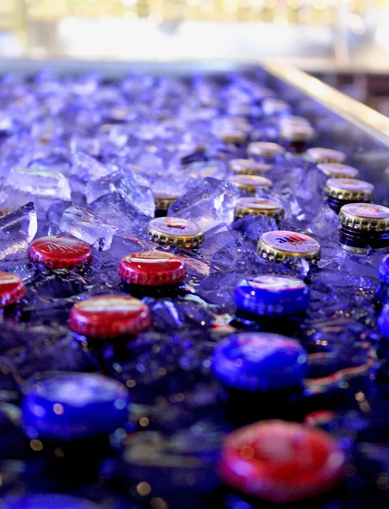 Colorful bottle caps submerged in blue-purple ice in a cooler.