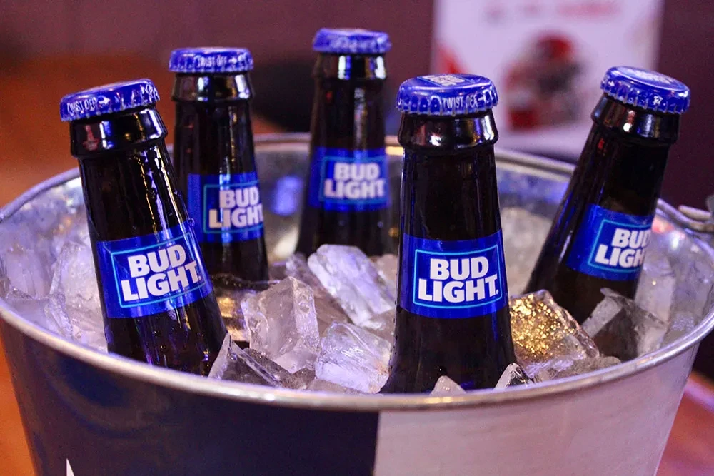 Five Bud Light beer bottles in a silver ice bucket with ice.