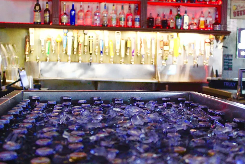 Iced drinks in a cooler, with beer taps and liquor bottles behind.