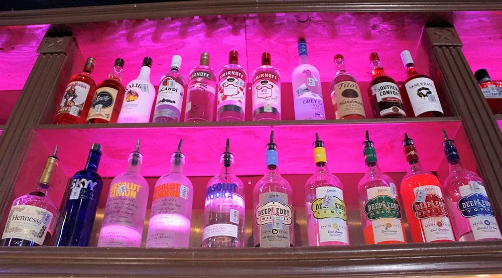 Pink-lit shelves displaying various liquor bottles with speed pourers.