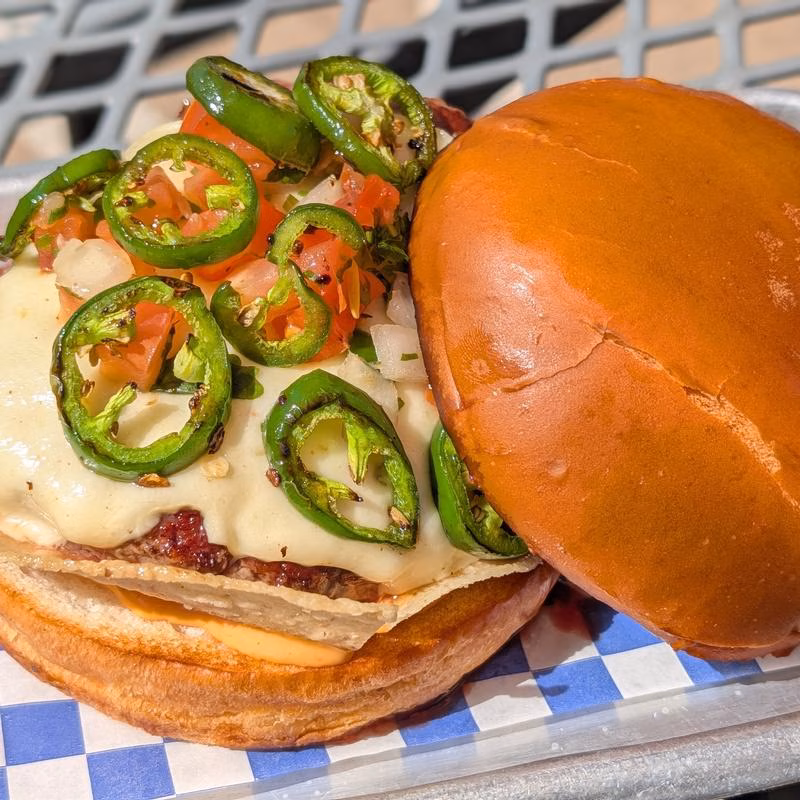 An open-faced burger with melted cheese, pico de gallo, and jalapeños.