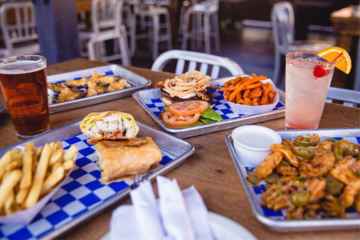 Metal trays of casual food, beer, and cocktails on a table.