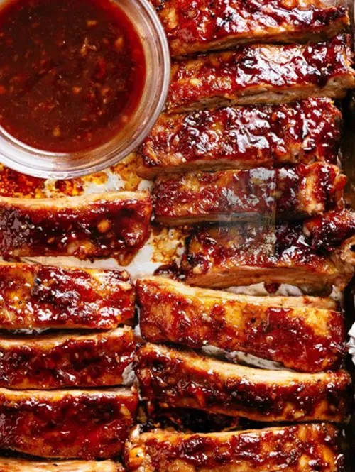 Overhead close-up of glistening individual BBQ ribs in reddish sauce.