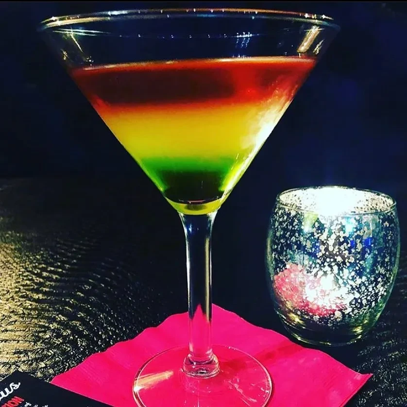 Three-layered red, yellow, green cocktail in a martini glass, dimly lit.