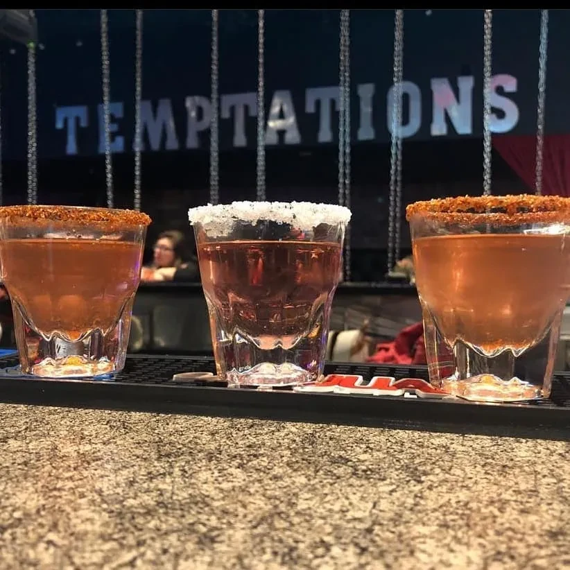 Three shot glasses with varied rims and liquids on a granite bar.