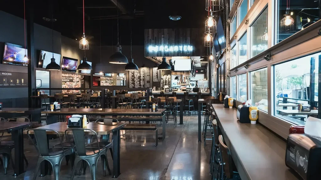 Empty modern industrial restaurant with bar, TVs, and large windows.