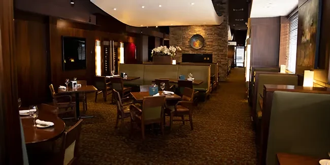 Restaurant dining room featuring green booths, stone fireplace, and dark wood walls.